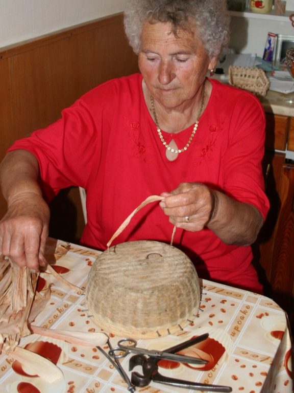 Zobraziť fotografiu Výrobkyňa pri pletení košíka zo stáčaného šúpolia na drevenej forme